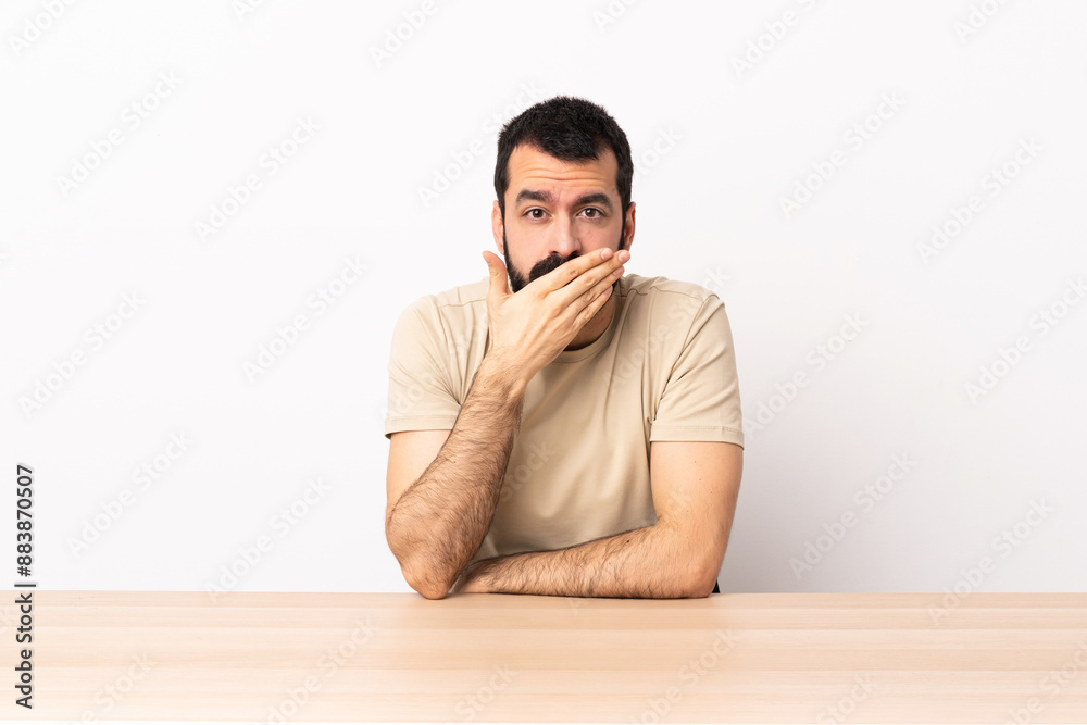 Caucasian man with beard in a table covering mouth with hand.
