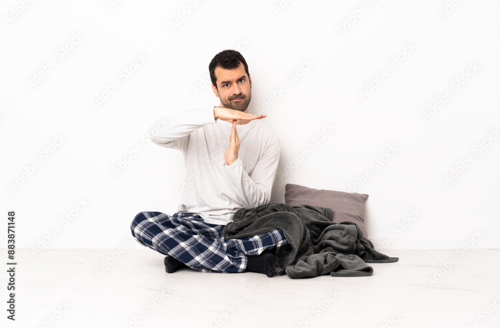Caucasian man in pajamas sitting on the floor at indoors making time out gesture Caucasian man in pajamas sitting on the floor at indoors making time out gesture