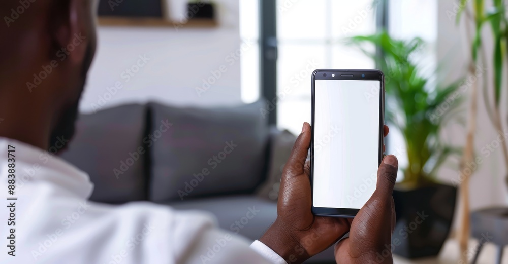 African American man using a smartphone with a blank screen while relaxing at home. African American man using a smartphone with a blank screen while relaxing at home.