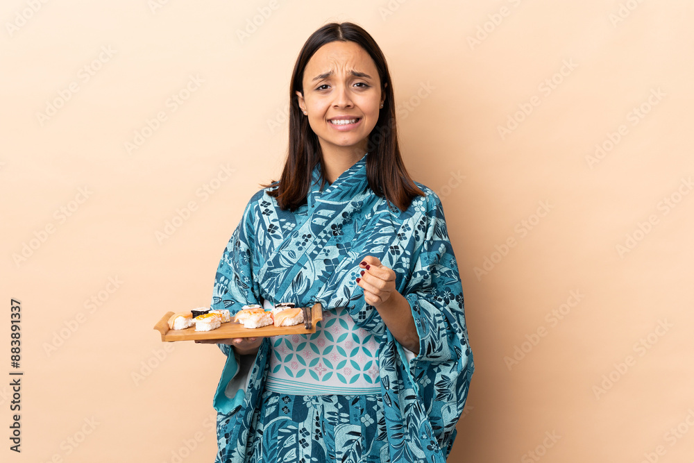 Woman wearing kimono and holding sushi over isolated background laughing Woman wearing kimono and holding sushi over isolated background laughing