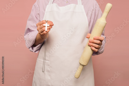 Woman cook with Catholic cross on studio pink background. Portrait of a female person in chef's clothing