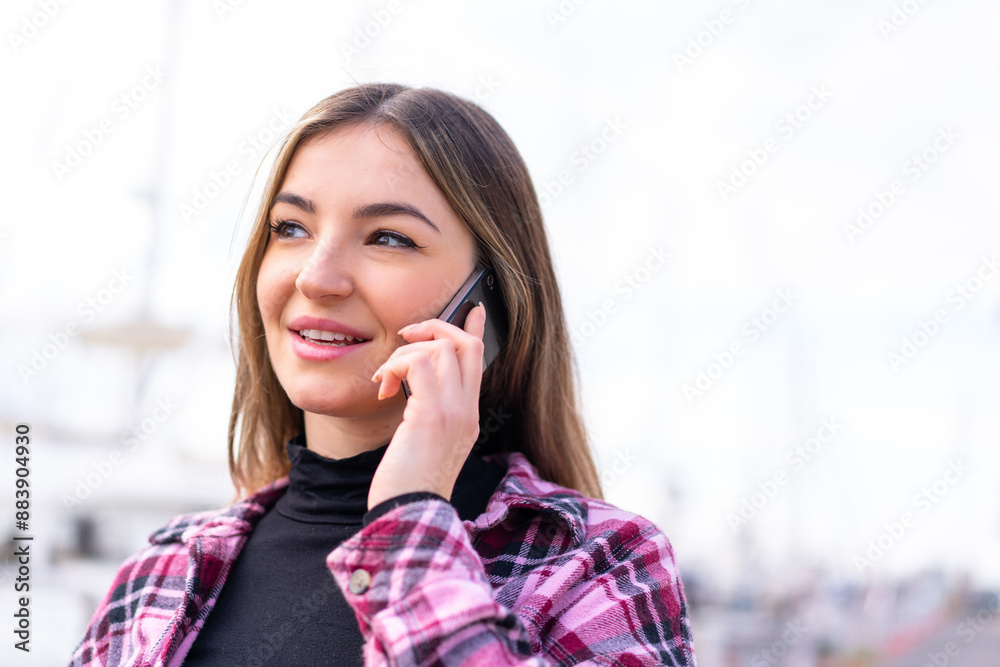 Young pretty Romanian woman at outdoors keeping a conversation with the mobile phone with someone