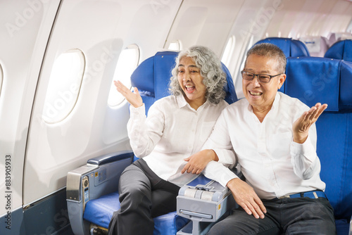 A mature couple enjoys a plane ride, seated near the window. They gaze out at the sky, savoring the view and the excitement of travel, creating cherished memories together.