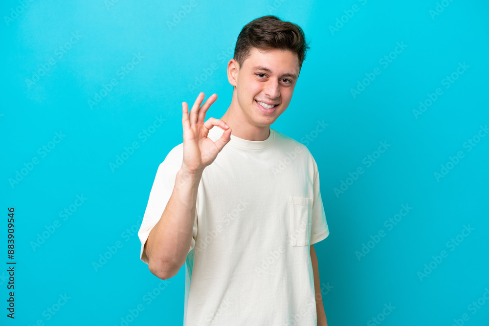 Young handsome Brazilian man isolated on blue background showing ok sign with fingers Young handsome Brazilian man isolated on blue background showing ok sign with fingers