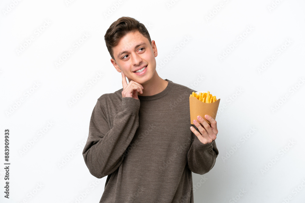 Young Brazilian man holding fried chips isolated on white background thinking an idea while looking up Young Brazilian man holding fried chips isolated on white background thinking an idea while looking up