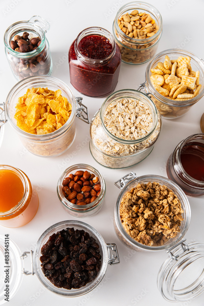 food storage and eating concept - close up of jars with oat, corn flakes, granola, cookies and spreads on white background food storage and eating concept - close up of jars with oat, corn flakes, granola, cookies and spreads on white background