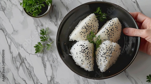 Onigiri with accompaniments in a black plate, with a hand holding, looks delicious on a clean white table background, typical Japanese food