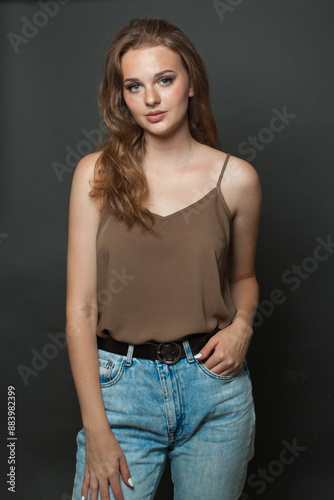 Casual young adult woman in silk top wearing light jacket standing against black studio wall background © artmim