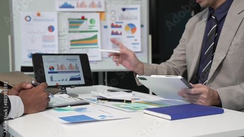 A collaborative meeting at an office desk focusing on teamwork, with discussions centered around financial charts and the sub-account management of work in process in production cost accounting.