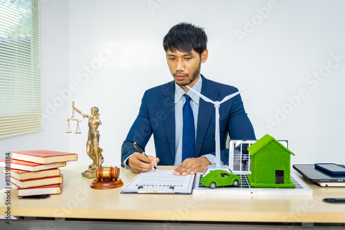 A male Asian lawyer in a formal suit works at his desk, focusing on contracts and legal matters, with a commitment to sustainability and reducing environmental impact. environmental law 2050