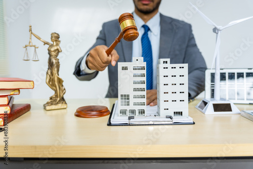 A male Asian lawyer in a formal suit works at his desk, focusing on contracts, legal matters, and urban planning issues such as building models, zoning, ordinances, and municipal regulations. photo