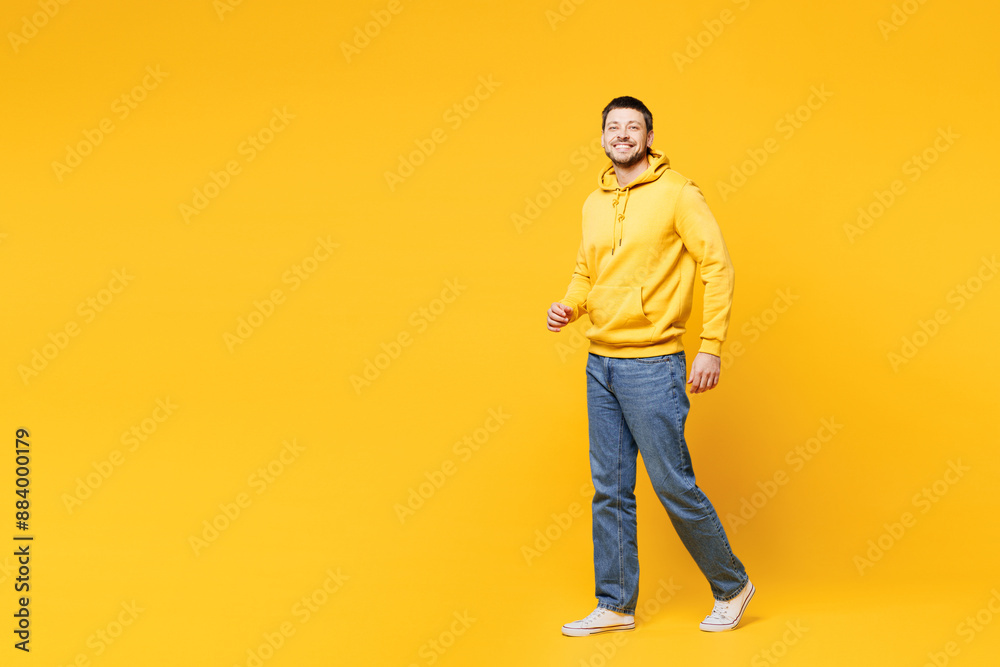 Full body side profile view young smiling cheerful happy man he wearing hoody casual clothes walking going looking camera isolated on plain yellow orange background studio portrait. Lifestyle concept. Full body side profile view young smiling cheerful happy man he wearing hoody casual clothes walking going looking camera isolated on plain yellow orange background studio portrait. Lifestyle concept.