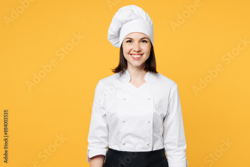 Young smiling happy cheerful professional chef cook baker woman she wear white shirt black apron uniform toque chefs hat look camera isolated on plain yellow background studio. Cooking food concept.