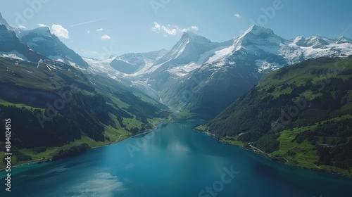 Stunning aerial view of snow-capped mountains and a serene blue lake surrounded by green valleys under a clear sky.