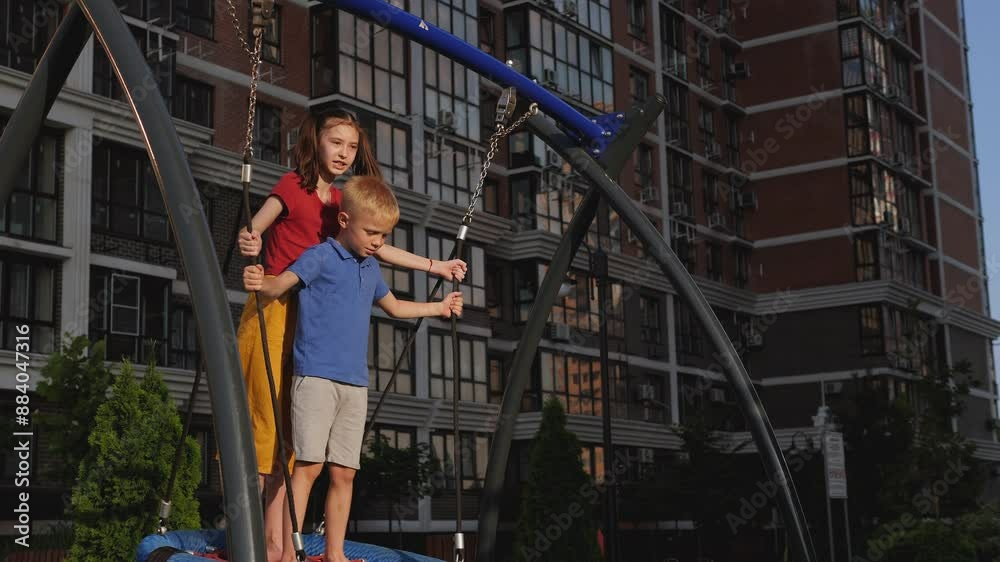 A little boy and a girl ride together on a round swing on a modern playground in the courtyard of a multi-storey building. A little boy and a girl ride together on a round swing on a modern playground in the courtyard of a multi-storey building.