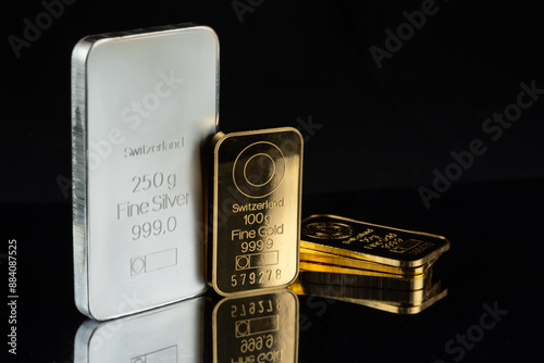 Gold and silver bars of various weights on a black mirror background. Selective focus.