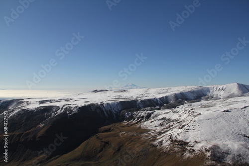 Breathtaking winter scenery with majestic snow-capped mountains glistening under the sun against a backdrop of a clear blue sky. Ideal for capturing the tranquil beauty of a winter wonderland.