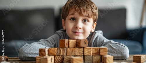  A young boy, seated at a table, gazes at the camera while holding a pile of wooden blocks before him