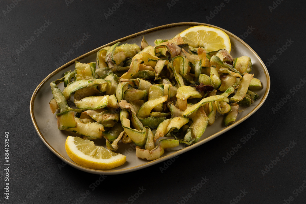 Fried zucchini with lemon on plate on black background. Fried zucchini with lemon on plate on black background.
