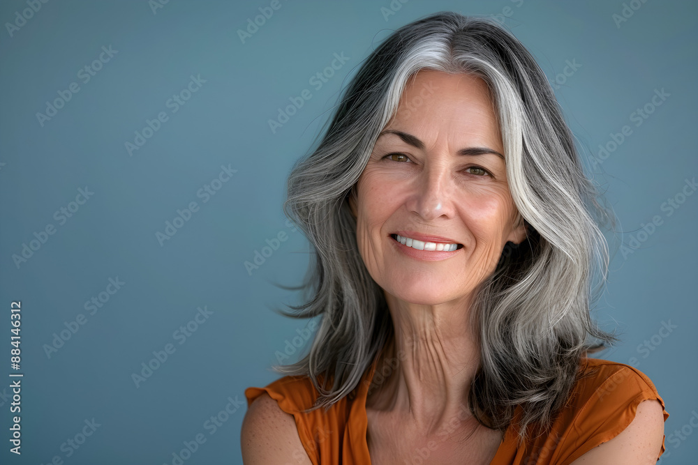 Fototapeta premium Portrait of a beautiful smiling senior woman on blue background, happy, relaxed adult grey-haired with copy space.