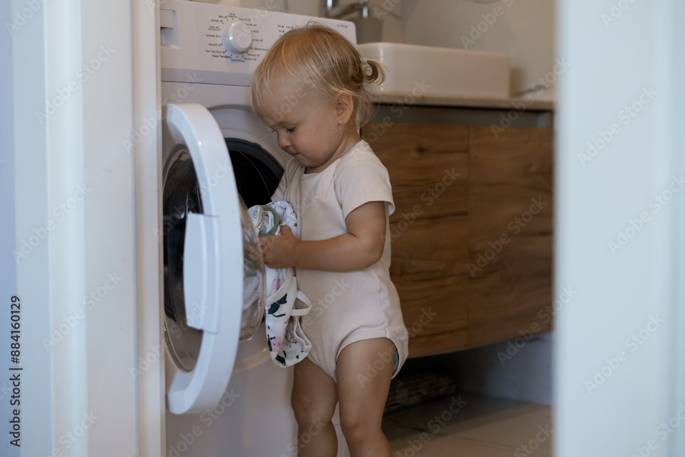 Two year old child doing household chores. Loading washing machine. Two year old child doing household chores. Loading washing machine.