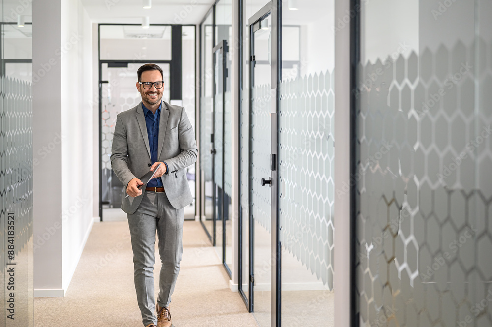 Portrait of smiling male accountant with eyeglasses and laptop walking confidently in office lobby Portrait of smiling male accountant with eyeglasses and laptop walking confidently in office lobby