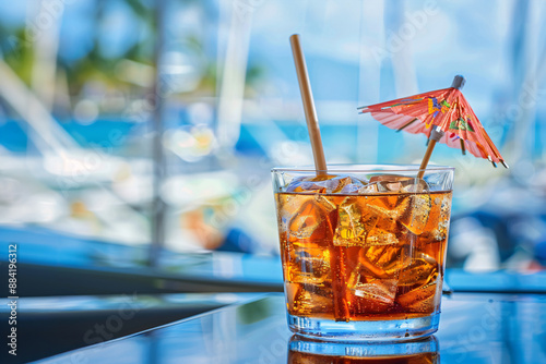 Cocktail with ice and umbrella on the background of the sea. Refreshing drink with ice and straw on the background of yachts. photo