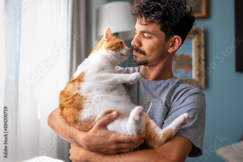 young man holds a white and brown cat with yellow eyes in his arms
