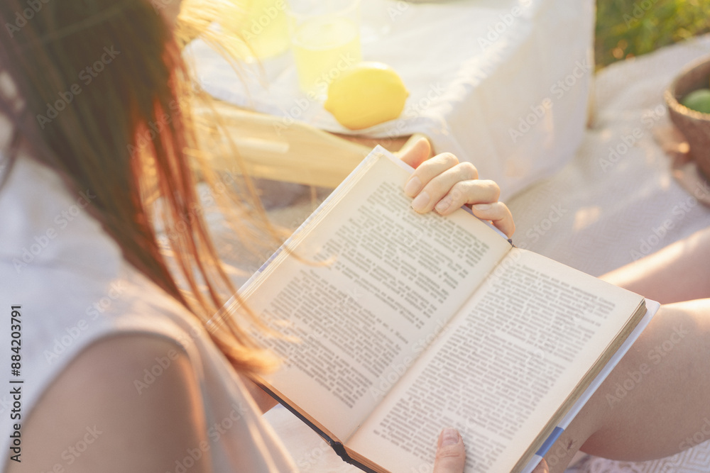 © Vladimir Razgulyaev - A woman finds peace and relaxation in nature while reading a book outdoors on a sunny day