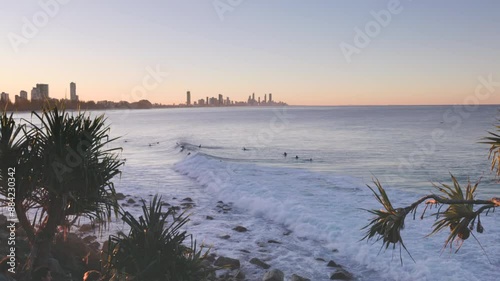 a wide panning shot of surfers riding a wave on a beautiful winter's sunset at burleigh heads in queensland, australia