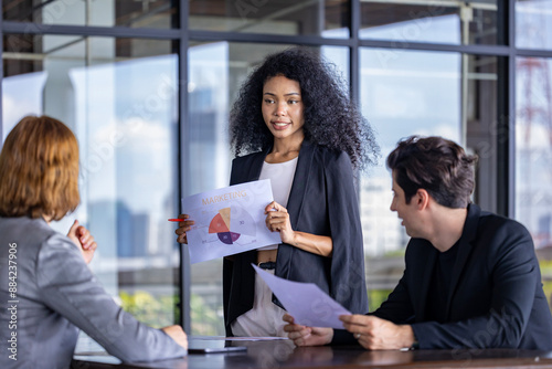 Young African woman sale manager is showing annual report chart to her colleagues in the executive meeting for next year plan with market share pie chart for global business and investment