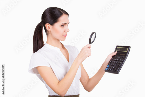 A woman is carefully studying a calculator using a magnifying glass in an office environment