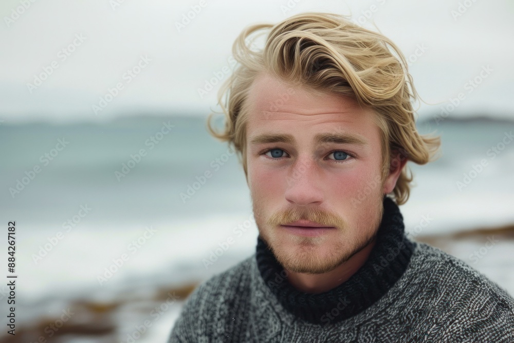 Handsome blond man in a grey sweater poses thoughtfully by the sea Handsome blond man in a grey sweater poses thoughtfully by the sea