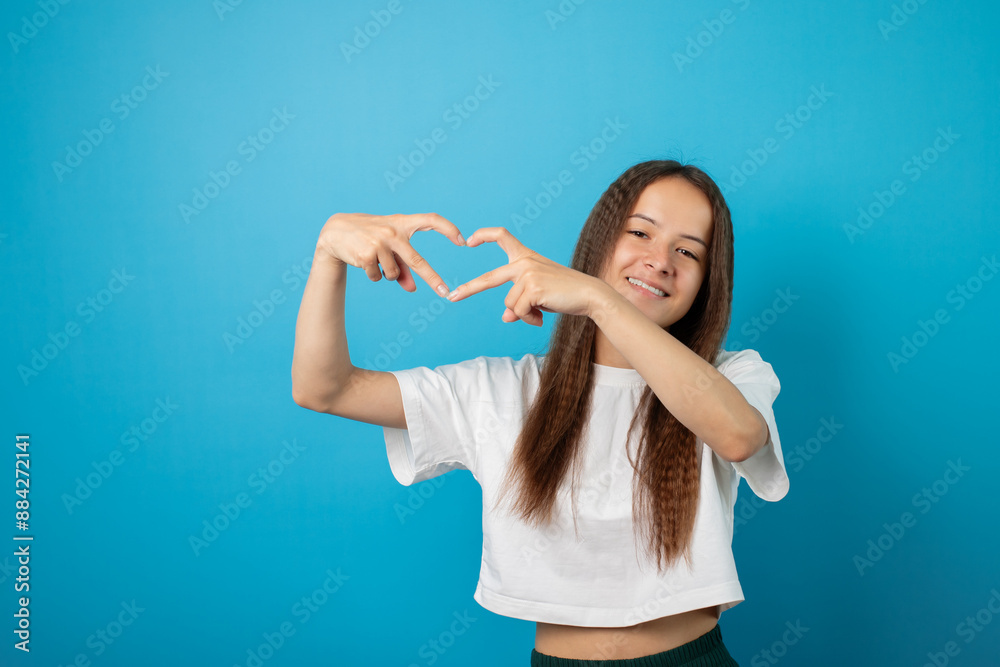 Teenager portrait on blue background, shows a heart sign with his fingers,young cute emotional student, cheerful female with attractive smile, happy youth posing Teenager portrait on blue background, shows a heart sign with his fingers,young cute emotional student, cheerful female with attractive smile, happy youth posing