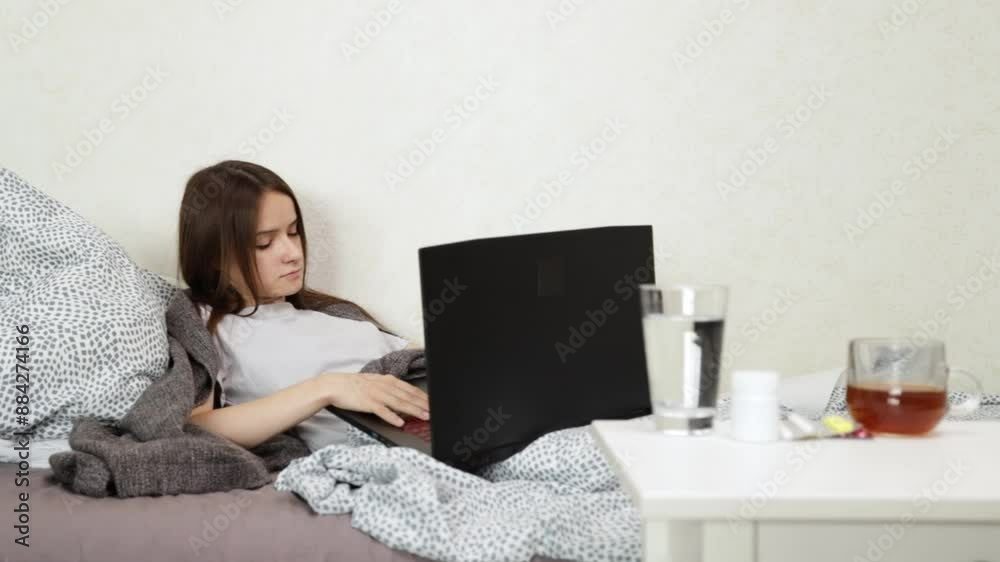 Teenager is sick, lying in bed with a laptop, student working on remote lessons, illness affecting education, online training during sickness. Teenager is sick, lying in bed with a laptop, student working on remote lessons, illness affecting education, online training during sickness.