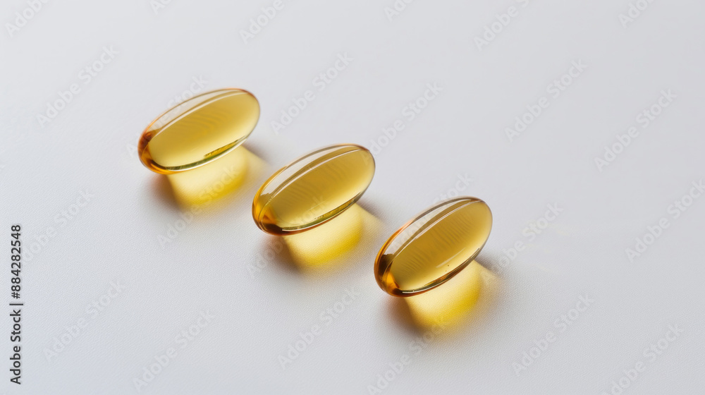 Three golden softgel capsules on a white background, glowing with a light reflection, symbolizing health and wellness supplements, vitamins, or omega-3 fish oil Three golden softgel capsules on a white background, glowing with a light reflection, symbolizing health and wellness supplements, vitamins, or omega-3 fish oil