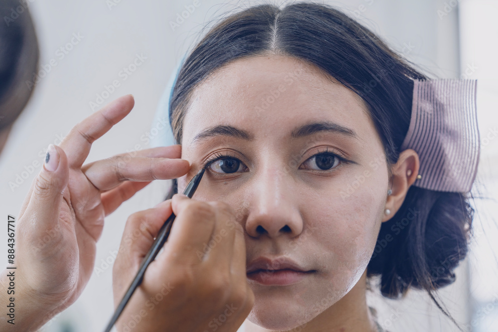 makeup artist makes up an Asian woman using eyeliner and using foundation and powder to make her skin look beautiful and fresh. makeup artist makes up an Asian woman using eyeliner and using foundation and powder to make her skin look beautiful and fresh.