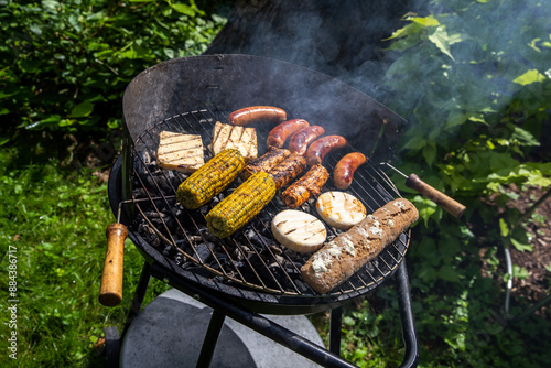 Ein Holzkohlegrill mit Würstchen Maiskolben Baguette,  und Grillkäse belegt. photo