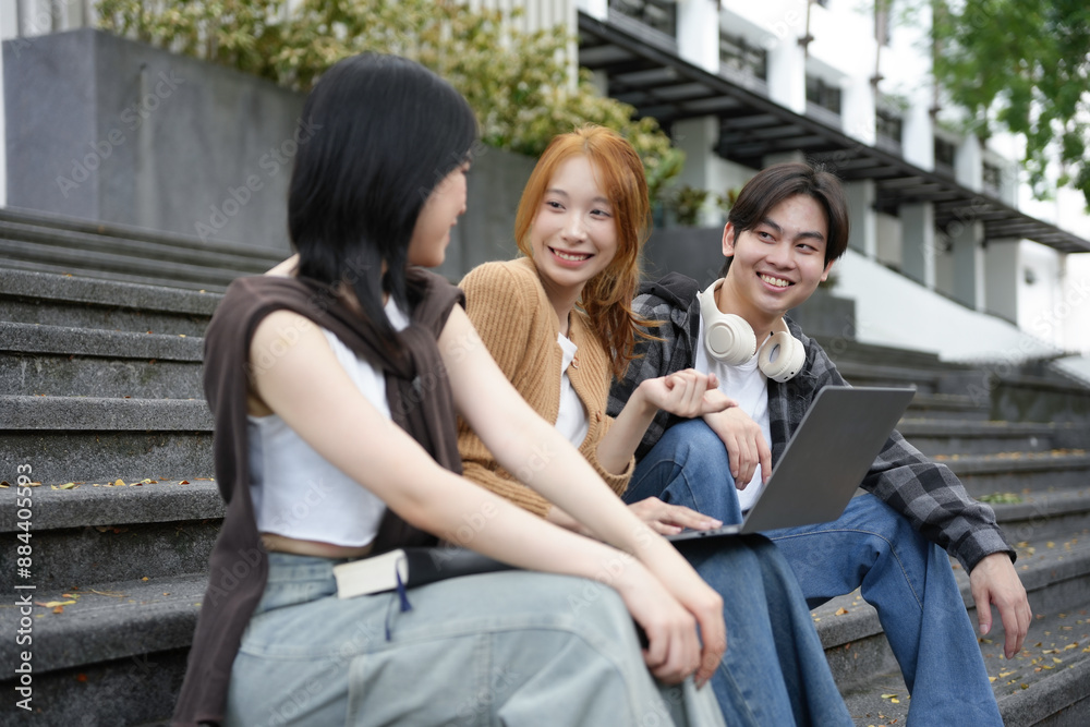 Three youths happily collaborate on a project outdoors, seated on steps and working on a laptop Three youths happily collaborate on a project outdoors, seated on steps and working on a laptop