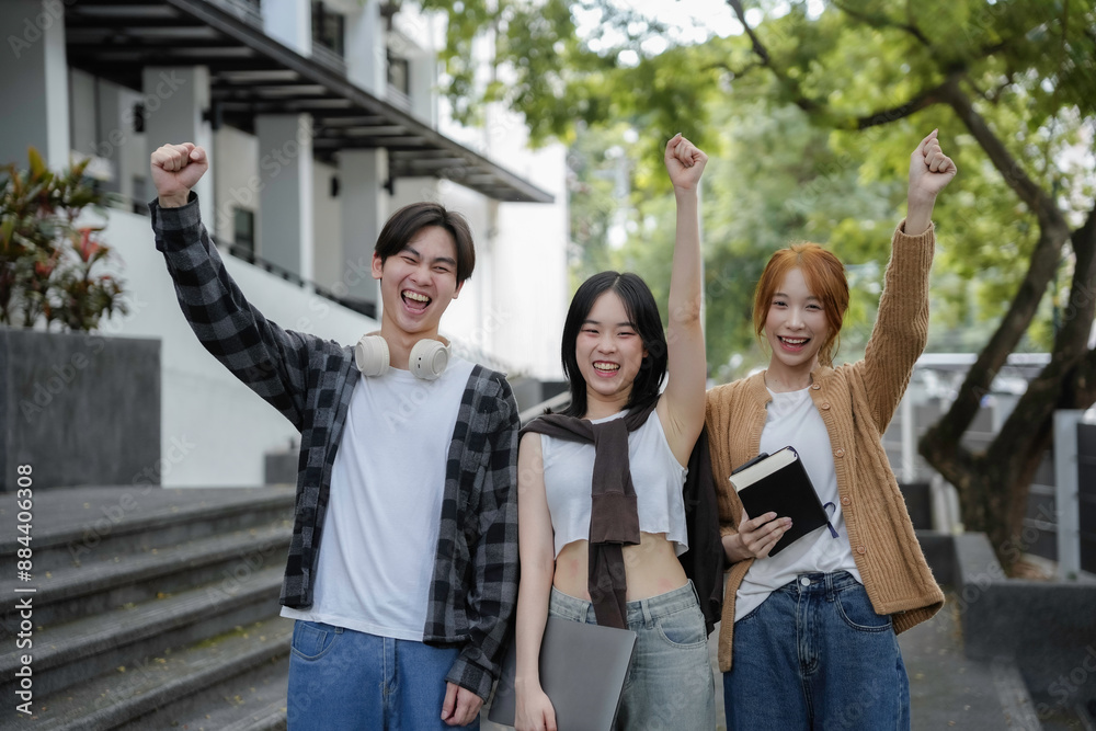 Obraz premium Three enthusiastic students triumph outside university building, raising their fists in joy and celebration