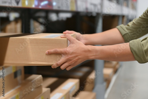 Obraz na plátně Hand of a person holding a cardboard box in a warehouse, illustrating the act of picking up or storing products