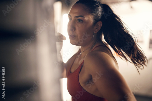 Fit young woman wearing a tank top and boxing gloves hitting a punching bag during boxing practice alone in a gym