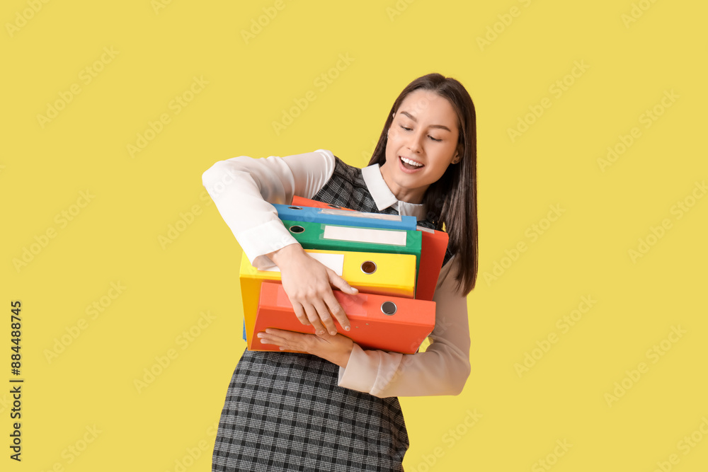 Young secretary holding office folders on yellow background Young secretary holding office folders on yellow background