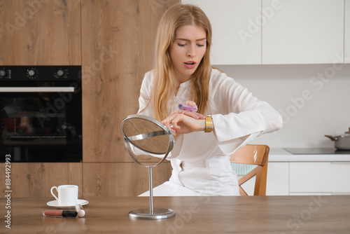 Hurrying young woman applying makeup while checking time at home