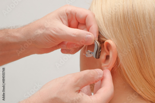 Doctor putting an hearing aid. The hands of a male audiologist trying on a hearing aid on a woman's ear. Helping technologies for people with disabilities