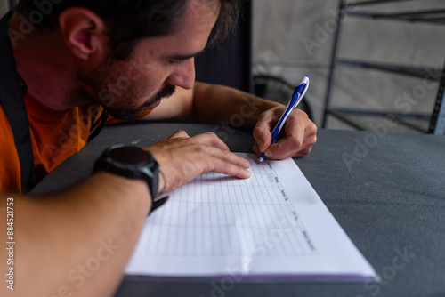 Man meticulously fills out a worksheet in a dimly lit room