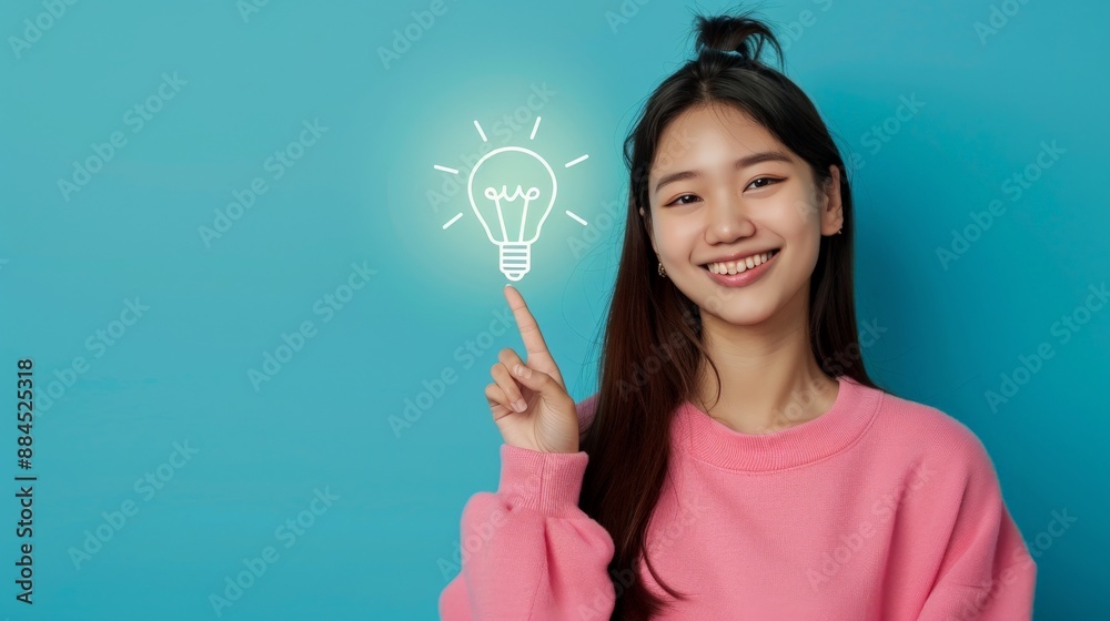A smiling woman in a pink sweater points to a glowing lightbulb A smiling woman in a pink sweater points to a glowing lightbulb