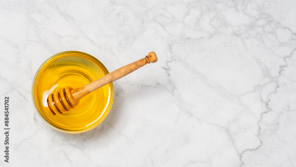 Honey in glass bowl with wooden honey dipper on marble background, top view Honey in glass bowl with wooden honey dipper on marble background, top view