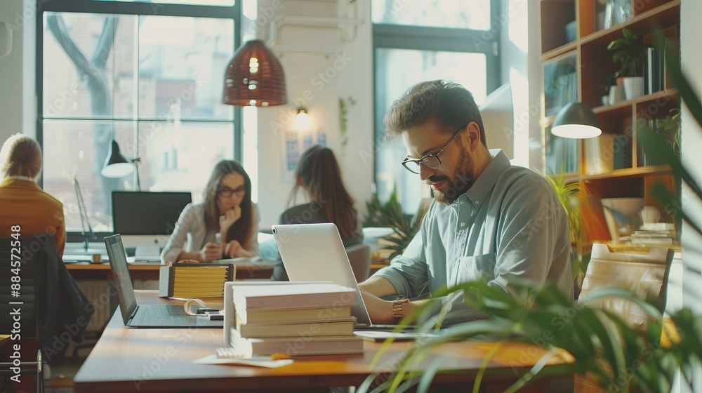 A modern office scene where people are working diligently on laptops, surrounded by stacks of books, plants, and stylish furnishings creating an energetic and productive atmosphere.