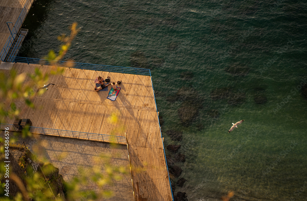 A beautiful view of wooden platform on a beach with people relaxing and birds flying across on a marina beach of Sorrento, Italy